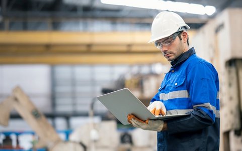 Occupational safety professional wearing a white helmet and blue jacket, using a laptop