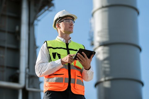 Quentic AI in action: Safety professional in high-visibility vest and hard hat using a tablet during an inspection at an industrial facility
